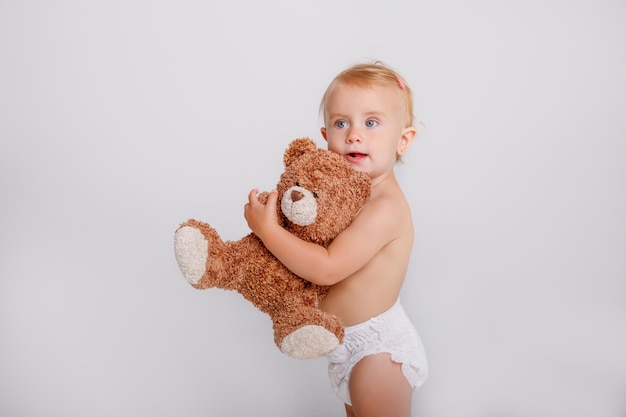 Babymädchen in der Windel, die Teddybären auf weißem Hintergrund hält