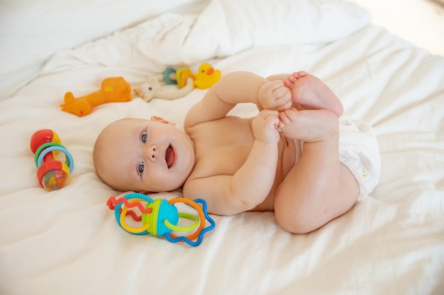 Babymädchen in einer Windel, die auf dem Bett mit Spielzeug liegt, rasselt Draufsicht