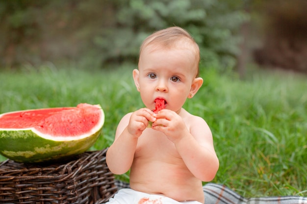 Babymädchen isst Wassermelone im Sommer draußen auf dem Rasen sitzend