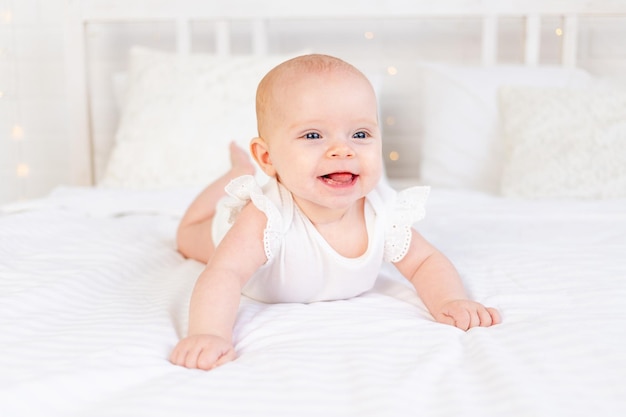 Babymädchen lächelt zu Hause auf einem weißen Baumwollbett auf dem Bauch liegend