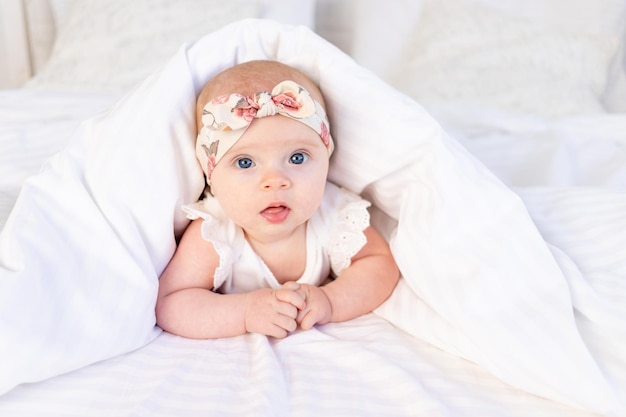 Babymädchen liegt unter einer Decke und lächelt auf einem weißen Baumwollbett zu Hause am Morgen des Neugeborenen