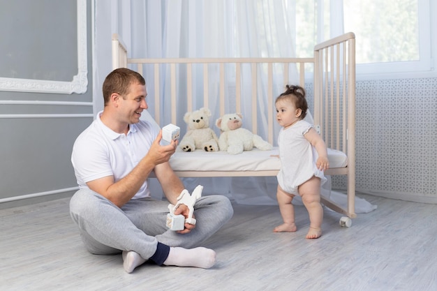 Babymädchen macht ihre ersten Schritte Papa bringt Baby bei, im Kindergarten zu gehen, glückliche Vaterschaft