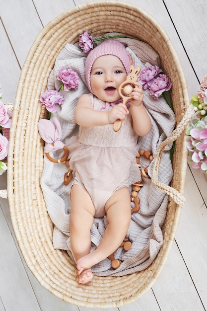 Babymädchen mit Blumenhut im Weidenkorb mit Holzrassel Postkarte Muttertag und Ostern Kinderschutztag Weltglückstag Lächelndes Kind