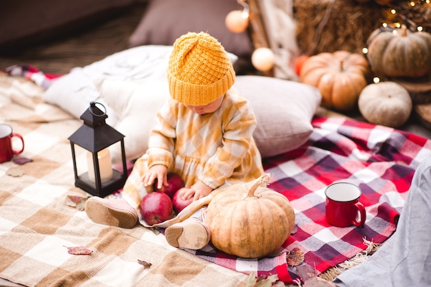 Babymädchen mit Strickmütze und stilvollem Kleid mit roten leckeren Äpfeln mit Kürbis