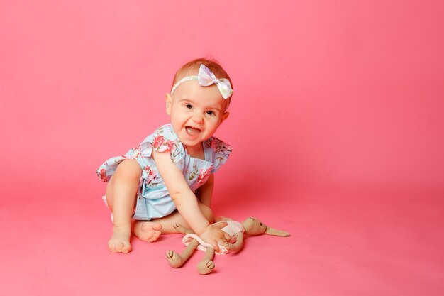 Babymädchenporträt in einem Kleid, das auf einem rosa Hintergrund sitzt