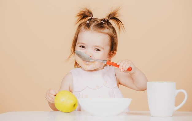 Babys, die gesunde Nahrung für ein Baby essen Erste Mahlzeit des Babys Das Kind isst alleine mit einem Löffel und einem Teller