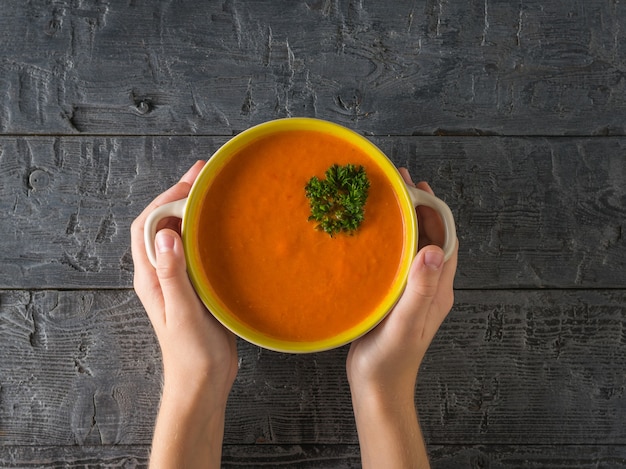 Babys Hände halten einen Topf mit frischer Sahnesuppe auf einem Holztisch. Suppe der vegetarischen Ernährung. Flach liegen. Der Blick von oben.