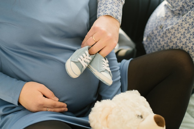 Babyschuhe, Jeansschuhe für das Baby in den Händen des zukünftigen Papstes, der die Schuhe an den Bauch der schwangeren Frau legt