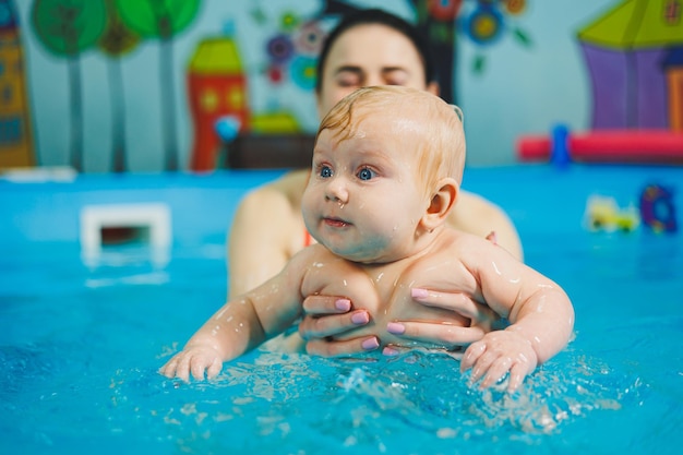 Babyschwimmen im Pool Einem neugeborenen Jungen mit einem Trainer das Schwimmen im Pool beibringen