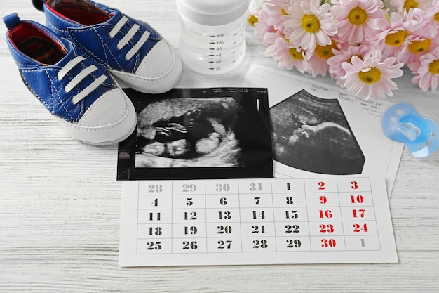 Babywartekonzept Ultraschallfoto und Kalender auf weißem Holzhintergrund