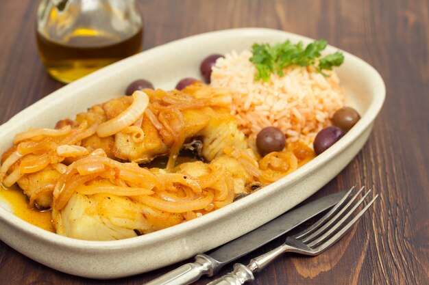 Bacalao frito con arroz hervido y aceite de oliva en un plato