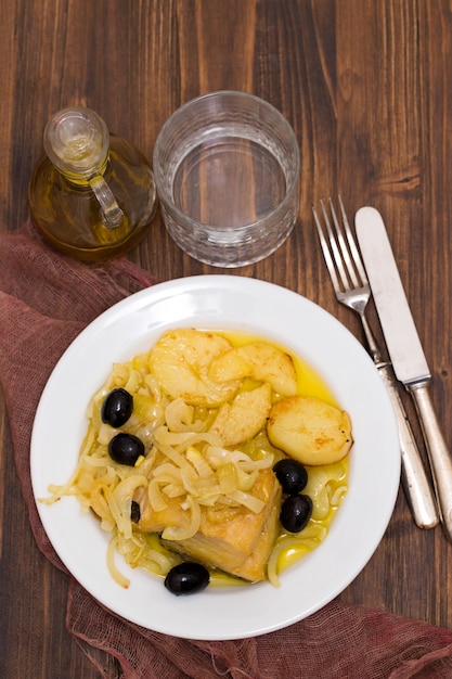 Bacalao frito con cebolla y patata en plato blanco