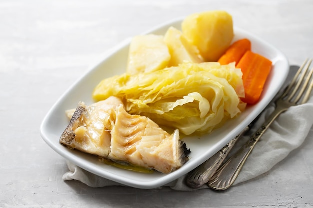 Bacalhau cozido com legumes cozidos e ovo no prato branco