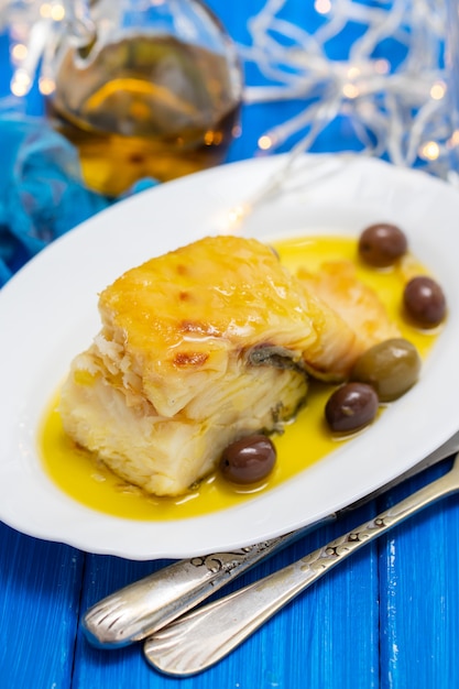 Bacalhau frito com azeitonas e azeite no prato branco