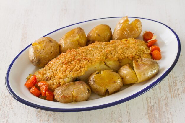 Bacalhau frito com pão e batata no prato na superfície de madeira branca