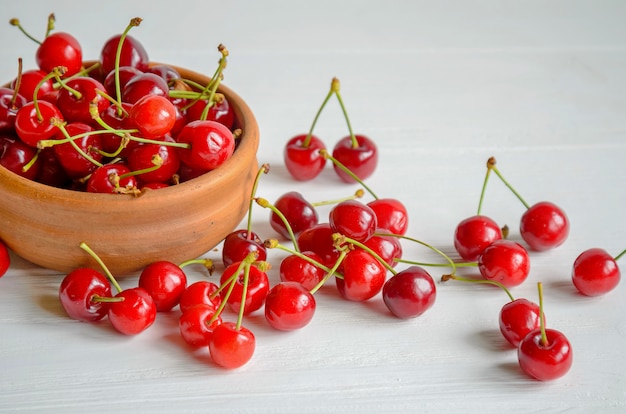 Bacia cerâmica marrom de cerejas frescas e saborosas em branco de madeira