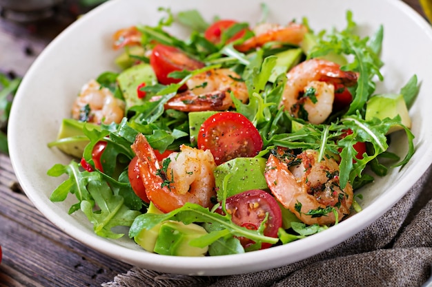 Bacia de salada fresca com camarão, tomate, abacate e rúcula no fim de madeira do fundo acima.