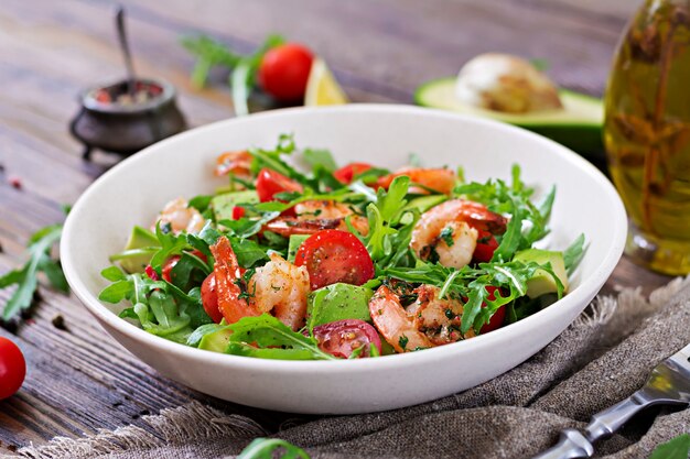 Bacia de salada fresca com camarão, tomate, abacate e rúcula no fim de madeira do fundo acima.