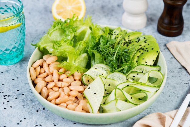 Bacia de salada verde do vegetariano com legumes frescos e feijões brancos enlatados em um fundo cinzento do concreto. Foto horizontal.