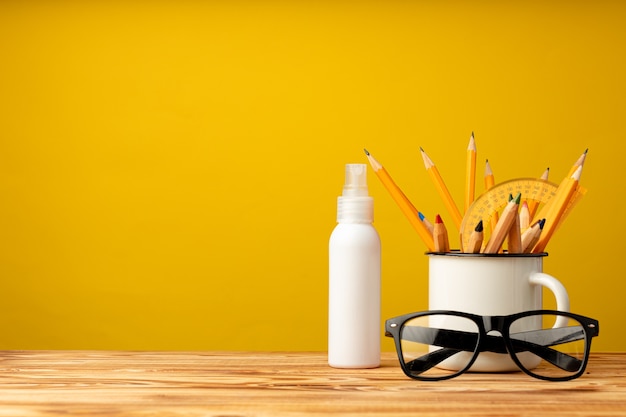 Back to School-Konzept mit Briefpapier in Tasse und Hand antiseptisches Spray