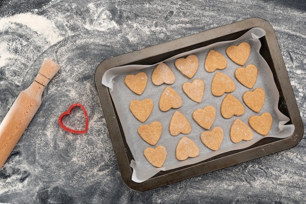 Backblech mit herzförmigen Keksen und hölzernem Nudelholz. Hausgemachtes Backen.