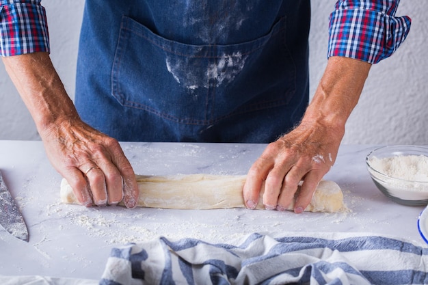 Backen Essen zu Hause gesunde Ernährung und Lifestyle-Konzept Senior Bäcker Mann kochen kneten frischen Teig mit Händen rollen mit Stift die Füllung auf dem Kuchen auf einem Küchentisch mit Mehl verteilen