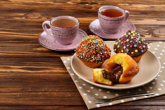 Backen mit Tee und Schokolade auf dem Tisch. Zwei Tassen Tee mit Cupcakes und Schokolade mit einem bunten Pulver auf dem Tisch.