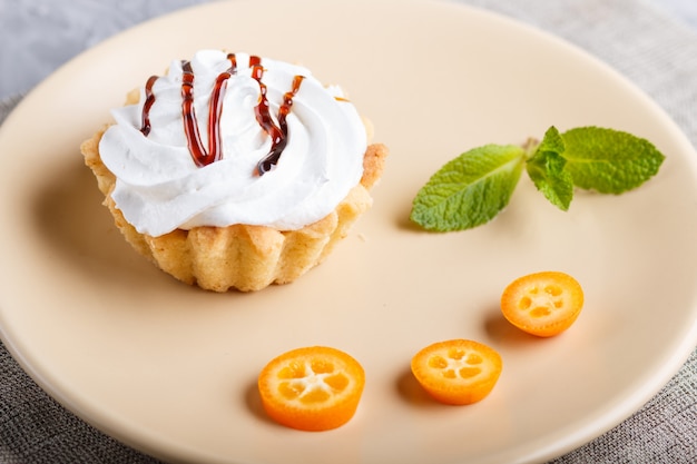 Backen Sie mit Schlagsahne auf einer hellbraunen Platte mit Scheiben der japanischen Orange und tadellosen Blättern auf Grau zusammen