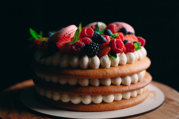 Backen Sie verziert mit Beeren auf einem hölzernen Stand auf Schwarzem zusammen