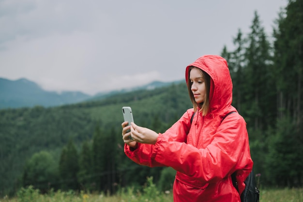 Backpacker in einer roten Regenjacke benutzt ihr Handy und fotografiert den Bergwald