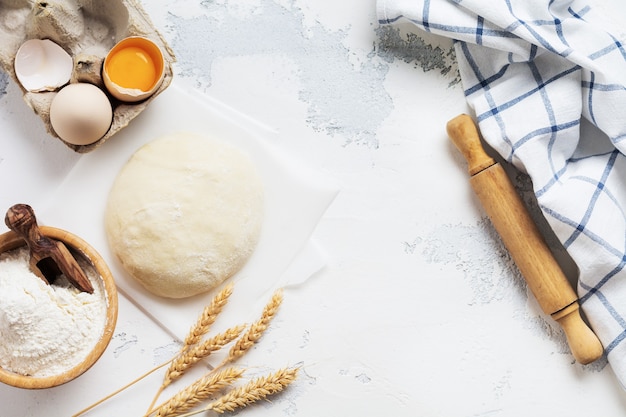 Backwand mit Teig und Zutaten für die Zubereitung von Nudeln oder Pfannkuchen, Eiern, Mehl, Wasser und Salz auf weißem rustikalem alten Tisch. Draufsicht.