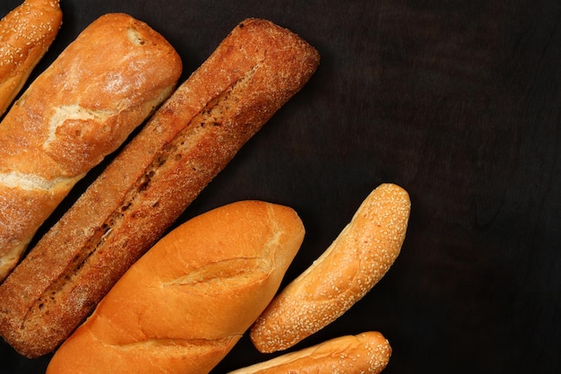 Backwaren auf dem Hintergrund einer hölzernen dunklen Tischplatte Ansicht Baguette Sesambrötchen und lange Laib frisch duftendes knuspriges Gebäck