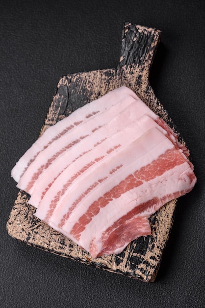 Foto bacon cru fresco cortado em fatias com especiarias salgadas e ervas em um fundo de concreto texturizado escuro