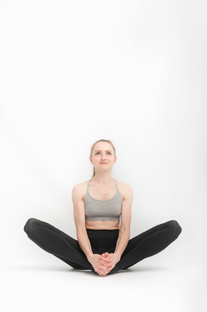 Baddha Konasana. Pose de ángulo enlazado. Hermosa mujer practica yoga. Chica se dedica a la aptitud y desarrolla su flexibilidad sobre fondo blanco. Marco vertical