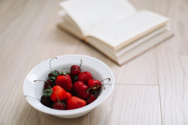 Badeanzug-Hutbuch und frische Süßkirschen und Erdbeeren auf Holzoberfläche