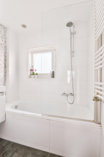 Badewanne mit Glasdusche in der Ecke neben Waschbecken und Spiegel in kleinem, hellem Badezimmer mit weißen Fliesenwänden