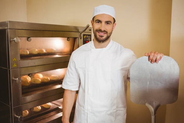 Bäcker, der an der Kamera neben Ofen lächelt