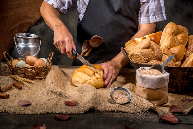 Bäcker, der Brot auf rustikalem Tisch schneidet.