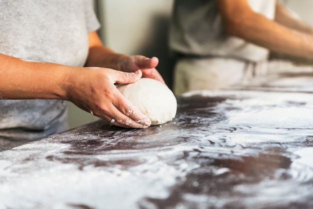 Bäcker, der Brot zubereitet. Nahaufnahme von Händen, die Teig kneten. Bäckerei-Konzept.