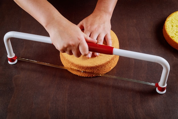 Bäcker, der die Oberseite des Kuchens mit einem gezackten Richtkuchen schneidet. Eine Torte backen.