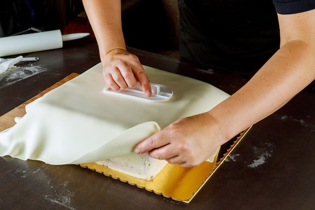 Bäcker, der quadratischen Kuchen mit weißem Fondant bedeckt. Technik der Kuchenherstellung.