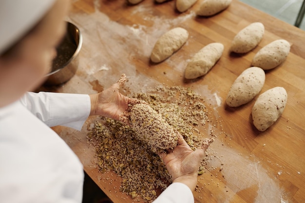 Bäcker formt Brotbagels, taucht Teig mit Samen und Haferflocken ein. Bäckerei-Haus-Konzept