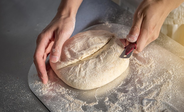 Bäcker schneidet den Teig mit einem Messer, bevor er zum Backen in den Ofen geht. Herstellung von Backwaren