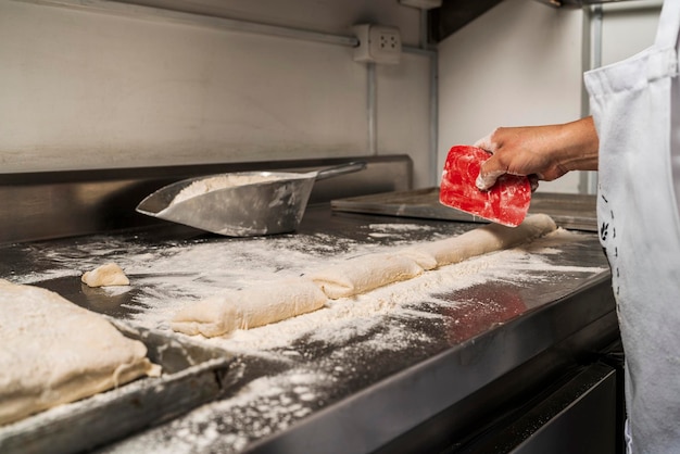 Bäcker schneidet in einer Küche eine Stange ungekochtes Brot in Stücke