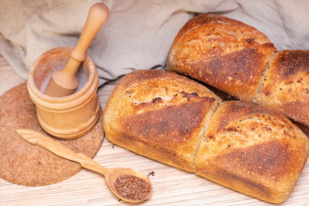 Bäckerei - goldene rustikale Brotkrusten. Frisches aromatisches Brot auf dem Tisch. Lebensmittelkonzept. Holzlöffel mit Leinsamen.