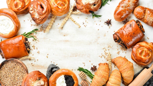 Bäckerei. Satz Brötchen mit Marmelade, Hüttenkäse, Mohn und Sesam auf weißem Holzhintergrund. Backen aus Roggen und Mehl. Ansicht von oben. Rustikaler Stil.