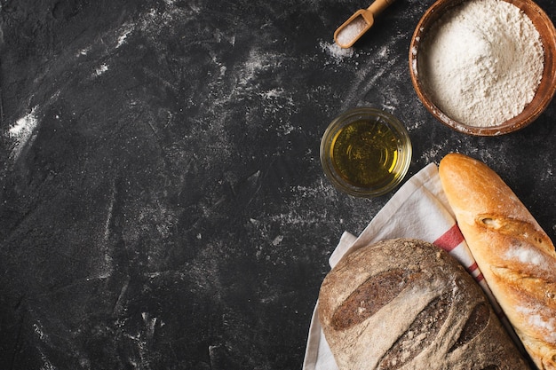 Bäckereikonzept mit Brotzutaten und Stoff auf schwarzem Hintergrund flach gelegt