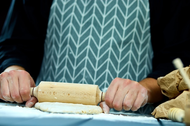 Bäckerhände, die frischen Teig mit Nudelholz auf Küchentisch vorbereiten