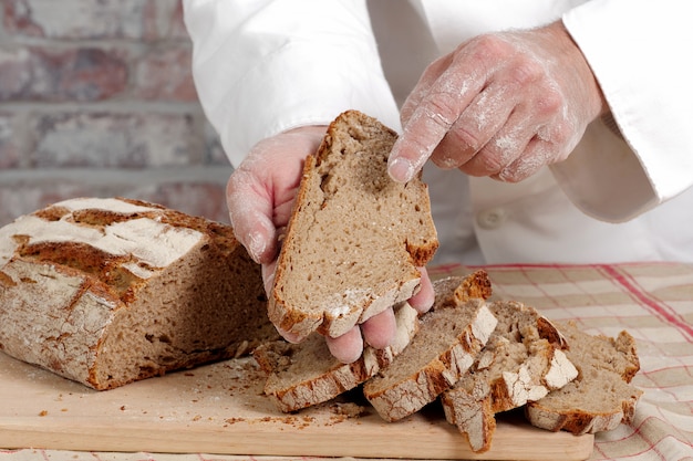 Bäckerhände mit frischem Brot auf hölzerner Tabelle