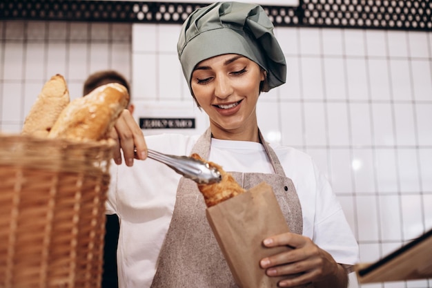 Bäckerin legt Croissant in eine Papiertüte